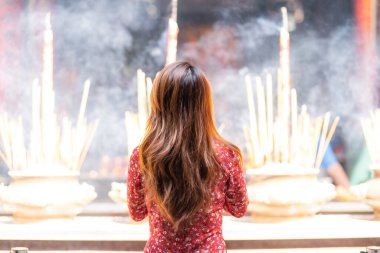 Vietnamese girl in traditional long dress or Ao Dai dress is praying with incense stick in the burning pot of a pagoda in Ho Chi Minh City, Vietnam. Tet holiday and New Year. . Tet holiday and New Year. Travel concept.