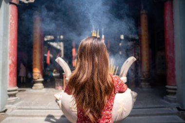 Vietnamese girl in traditional long dress or Ao Dai dress is praying with incense stick in the burning pot of a pagoda in Ho Chi Minh City, Vietnam. Tet holiday and New Year. . Tet holiday and New Year. Travel concept.