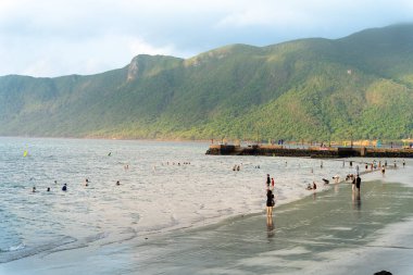 Con Dao Adası, Vietnam - 01 Mayıs 2023: Ünlü Con Dao sahilinde deniz dalgalarının tadını çıkaran turistler. Seyahat ve manzara konsepti.