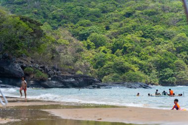 Con Dao Adası, Vietnam - 01 Mayıs 2023: Con Dao Adası, Vietnam 'daki Güzel Baraj Trau Sahili. Dalgalı kıyı manzarası, açık gökyüzü ve yol, mavi deniz, turistler ve dağ.