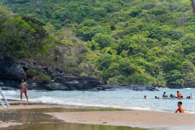 Con Dao Adası, Vietnam - 01 Mayıs 2023: Con Dao Adası, Vietnam 'daki Güzel Baraj Trau Sahili. Dalgalı kıyı manzarası, açık gökyüzü ve yol, mavi deniz, turistler ve dağ.