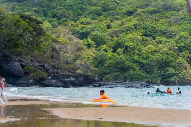 Con Dao Adası, Vietnam - 01 Mayıs 2023: Con Dao Adası, Vietnam 'daki Güzel Baraj Trau Sahili. Dalgalı kıyı manzarası, açık gökyüzü ve yol, mavi deniz, turistler ve dağ.
