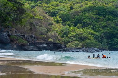 Con Dao Adası, Vietnam - 01 Mayıs 2023: Con Dao Adası, Vietnam 'daki Güzel Baraj Trau Sahili. Dalgalı kıyı manzarası, açık gökyüzü ve yol, mavi deniz, turistler ve dağ.
