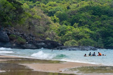 Con Dao Adası, Vietnam - 01 Mayıs 2023: Con Dao Adası, Vietnam 'daki Güzel Baraj Trau Sahili. Dalgalı kıyı manzarası, açık gökyüzü ve yol, mavi deniz, turistler ve dağ.