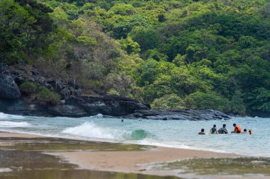 Con Dao Adası, Vietnam - 01 Mayıs 2023: Con Dao Adası, Vietnam 'daki Güzel Baraj Trau Sahili. Dalgalı kıyı manzarası, açık gökyüzü ve yol, mavi deniz, turistler ve dağ.