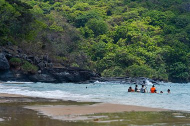 Con Dao Adası, Vietnam - 01 Mayıs 2023: Con Dao Adası, Vietnam 'daki Güzel Baraj Trau Sahili. Dalgalı kıyı manzarası, açık gökyüzü ve yol, mavi deniz, turistler ve dağ.