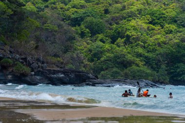 Con Dao Adası, Vietnam - 01 Mayıs 2023: Con Dao Adası, Vietnam 'daki Güzel Baraj Trau Sahili. Dalgalı kıyı manzarası, açık gökyüzü ve yol, mavi deniz, turistler ve dağ.