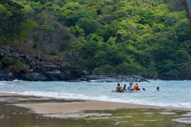 Con Dao Adası, Vietnam - 01 Mayıs 2023: Con Dao Adası, Vietnam 'daki Güzel Baraj Trau Sahili. Dalgalı kıyı manzarası, açık gökyüzü ve yol, mavi deniz, turistler ve dağ.
