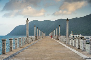 Con Son kasabasındaki yeni Con Dao yolcu limanının manzarası. Huzurlu bir Con Dao Adası, Vietnam. Dalgalı kıyı manzarası, kıyı şeridi, açık gökyüzü, mavi deniz, turistler ve dağ. Seyahat ve manzara konsepti.