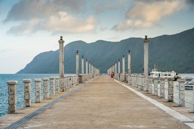Con Son kasabasındaki yeni Con Dao yolcu limanının manzarası. Huzurlu bir Con Dao Adası, Vietnam. Dalgalı kıyı manzarası, kıyı şeridi, açık gökyüzü, mavi deniz, turistler ve dağ. Seyahat ve manzara konsepti.