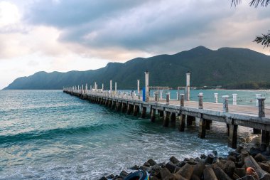 Con Son kasabasındaki yeni Con Dao yolcu limanının manzarası. Huzurlu bir Con Dao Adası, Vietnam. Dalgalı kıyı manzarası, kıyı şeridi, açık gökyüzü, mavi deniz, turistler ve dağ. Seyahat ve manzara konsepti.