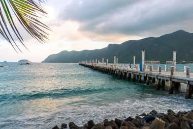 Con Son kasabasındaki yeni Con Dao yolcu limanının manzarası. Huzurlu bir Con Dao Adası, Vietnam. Dalgalı kıyı manzarası, kıyı şeridi, açık gökyüzü, mavi deniz, turistler ve dağ. Seyahat ve manzara konsepti.