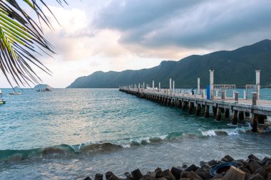 Con Son kasabasındaki yeni Con Dao yolcu limanının manzarası. Huzurlu bir Con Dao Adası, Vietnam. Dalgalı kıyı manzarası, kıyı şeridi, açık gökyüzü, mavi deniz, turistler ve dağ. Seyahat ve manzara konsepti.