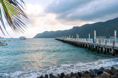 Con Son kasabasındaki yeni Con Dao yolcu limanının manzarası. Huzurlu bir Con Dao Adası, Vietnam. Dalgalı kıyı manzarası, kıyı şeridi, açık gökyüzü, mavi deniz, turistler ve dağ. Seyahat ve manzara konsepti.