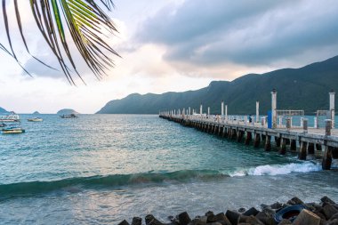 Con Son kasabasındaki yeni Con Dao yolcu limanının manzarası. Huzurlu bir Con Dao Adası, Vietnam. Dalgalı kıyı manzarası, kıyı şeridi, açık gökyüzü, mavi deniz, turistler ve dağ. Seyahat ve manzara konsepti.