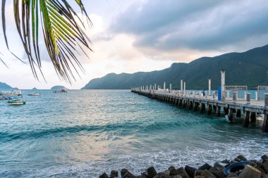 Con Son kasabasındaki yeni Con Dao yolcu limanının manzarası. Huzurlu bir Con Dao Adası, Vietnam. Dalgalı kıyı manzarası, kıyı şeridi, açık gökyüzü, mavi deniz, turistler ve dağ. Seyahat ve manzara konsepti.