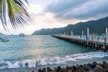 Con Son kasabasındaki yeni Con Dao yolcu limanının manzarası. Huzurlu bir Con Dao Adası, Vietnam. Dalgalı kıyı manzarası, kıyı şeridi, açık gökyüzü, mavi deniz, turistler ve dağ. Seyahat ve manzara konsepti.
