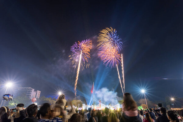 Pleiku city, Vietnam - 9 Feb 2024: New Year - people watch the beautiful colorful fireworks and lights in the night sky and wish Happy Tet Holiday, far away is Vietnam Flag and Ho Chi Minh statue