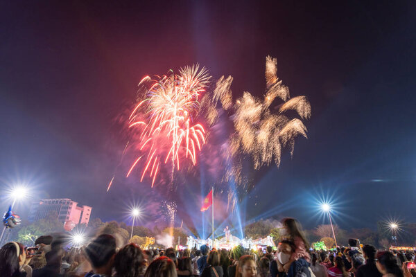 Pleiku city, Vietnam - 9 Feb 2024: New Year - people watch the beautiful colorful fireworks and lights in the night sky and wish Happy Tet Holiday, far away is Vietnam Flag and Ho Chi Minh statue