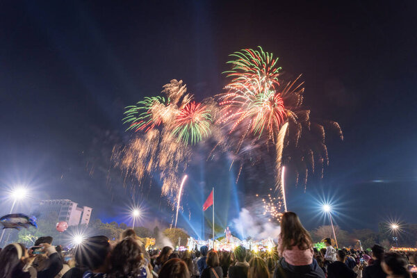 Pleiku city, Vietnam - 9 Feb 2024: New Year - people watch the beautiful colorful fireworks and lights in the night sky and wish Happy Tet Holiday, far away is Vietnam Flag and Ho Chi Minh statue