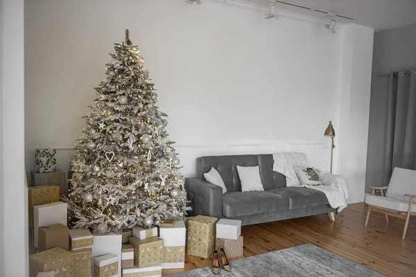 时尚时髦的斯堪的纳维亚内陆 在灰色的沙发旁边有一棵巨大的被雪覆盖的 奢华的人造圣诞树 木制层压板 礼物包在白色的金制工艺纸与装饰品 — 图库照片