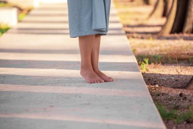 Womens feet barefoot on concrete floor in park with light shadow from forest. Gentle foot care pedicure. Laser hair removal. Spa masks for soft heels. Copy space. Taking care of yourself in the summer