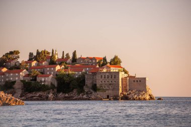 Panoramic view of Sveti Stefan in Montenegro at pink sunset. Famous tourist place near Budva. Natural beautiful island, with terracotta roofs among the turquoise sea. Copy space, wallpaper background