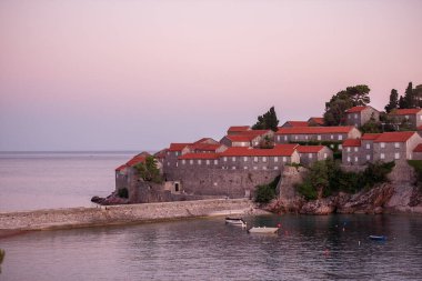 Panoramic view of Sveti Stefan in Montenegro at pink sunset. Famous tourist place near Budva. Natural beautiful island, with terracotta roofs among the turquoise sea. Copy space, wallpaper background