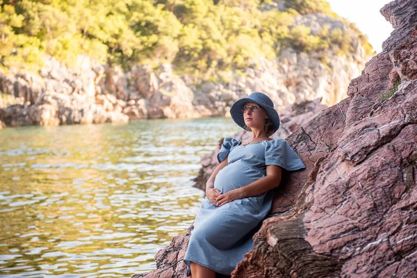 Middle Aged Pregnant Woman Blue Dress Hat Sits Rock Sea — Stok Foto