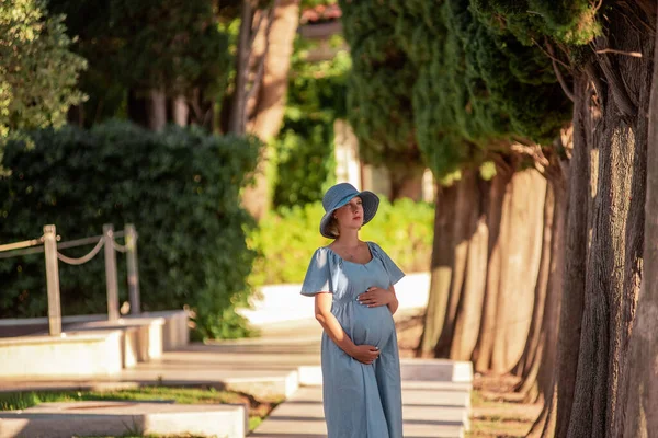 松林の中でロマンチックな中年の妊婦の肖像画を閉じます 千年の母親の帽子になるために 青いドレスは腹の中で赤ん坊を抱擁する 妊娠中の旅行の概念 モンテネグロのロイヤルビーチ — ストック写真