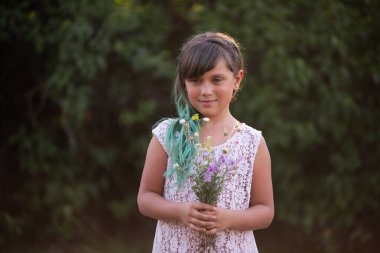 Yeşil saçlı kız botanik arka planda bir buket kır çiçeği tutuyor ve kameraya bakıyor. Annemiz için doğal bir hediye. Parlak çeşitlilik tarzında Z jenerasyonu. Uzayı kopyala Gülümseyen çocuk