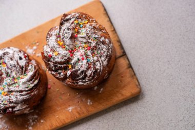 Hafif ahşap arka planda Paskalya Kraffini. Şekerli meyveli kek, kuru üzüm, çikolata, fındık, üzerine pudra şekeri, yenilebilir süslemeler. Köy usulü pişirme, servis. Uzayı kopyala, taklit et