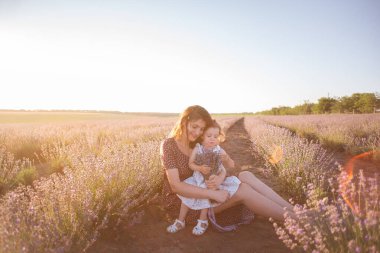 Küçük kızıyla mor lavanta tarlasında oturan esmer anne portresi. Kırsal kesimdeki genç kadın sevgiyle sarılıyor, kızı öpüyor. Alerji, seyahat, bekar ebeveyn kavramı. Boşluğu kopyala