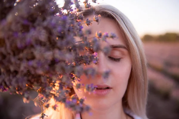 顔の前に紫色のラベンダーの花束と若い女性のクローズアップ肖像画 日没の光線でメイクせずにきれいな肌を持つブロンドの千年紀の女の子 アレルギーの概念 アロマオイルナチュラル香水 — ストック写真