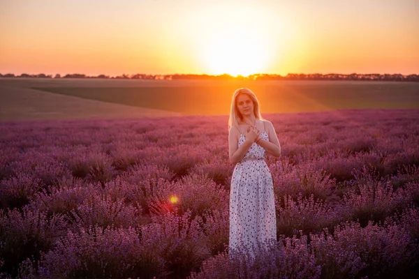 若いブロンドの女性は日没時に紫色のフィールドの行の間を歩く 田舎を旅行しなさい アレルギー 自由の概念 子供はロマンチックな女の子です 日没の日差しに照らされた スペースのコピー — ストック写真