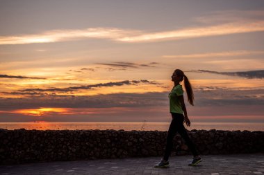 Genç bir kadın sabah antrenmandan önce ısınır. Güneşin doğuşunda deniz kenarında spor giyimli bir kadın. Akıl sağlığı, vücut sporu. Sabah rutini, kişisel bakım. Sağlıklı fitness