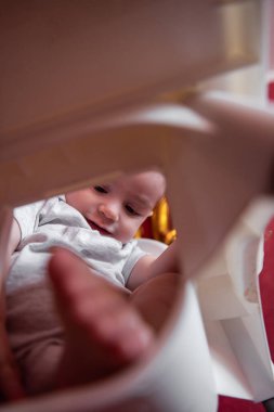 Şenlik şapkalı küçük bir çocuğun portresi kumaş bayraklarla çocuk koltuğunda oturuyor. Kırmızı izole edilmiş arka planda altın renkli balonları olan çocuk tatilini evde kutlayan duvar örüyor.