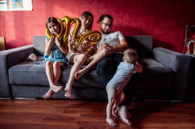 Şenlik şapkalı küçük kız kafasını folyo balon 1 'e sıkıştırdı. Mutlu, çeşitli bir ailenin portresi. Bir yıllık bebek için eğleniyorlar. Evde doğum günü partisi. Yaşam tarzı atmosferi