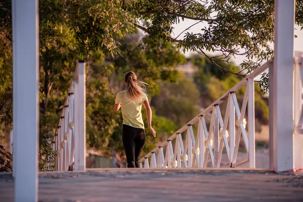 stock image Young woman in sportswear is exercising, jogging on wooden stairs in the rays of the dawn sun. Going in for sports on street of the city. Girl posing in the concept of sport, fitness. Morning routine