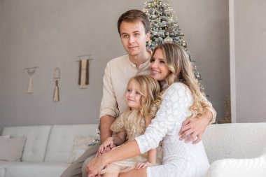 Noel ağacının yanında neşeli, mutlu bir ailenin yakın plan portresi. Anne, baba, küçük kızın kucaklaşması. Sıcak, şık bir tatil havası. Yeni yıl için parlak bir parti.