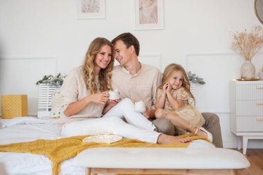 Komik anne baba, beyaz bardaklardan çıkan şekerlemelerle kakao içiyor ve tatlı kızına bakıyor. Noel arifesi, sıcak bir tatil. Genç aile kucaklaşmaları, kahkahalar. Kıvırcık kız kameraya bakıyor.