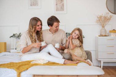 Komik anne baba, beyaz bardaklardan çıkan şekerlemelerle kakao içiyor ve tatlı kızına bakıyor. Noel arifesi, sıcak bir tatil. Genç aile kucaklaşmaları, kahkahalar. Kıvırcık kız kameraya bakıyor.