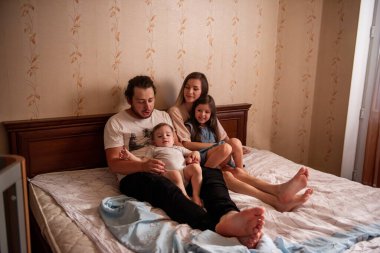 Sabahın köründe pencereden güzel bir ailenin uzun menzilli fotoğrafını çektim. Anneye, babaya, kıza, oğlana dokundum. Aile hafta sonu, evde rahatlama. Aile yatak odası manzarası