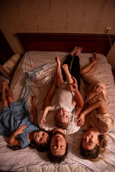 stock image Top view of a cheerful family lying on the bed in the morning. Stylish mother and eldest daughter hug their father from both sides, the baby son crawls on the mans stomach. Domestic life, lifestyle