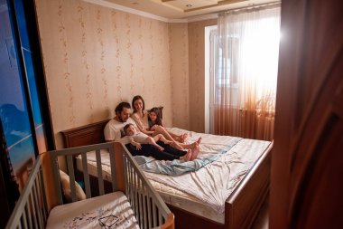 Sabahın köründe pencereden güzel bir ailenin uzun menzilli fotoğrafını çektim. Anneye, babaya, kıza, oğlana dokundum. Aile hafta sonu, evde rahatlama. Aile yatak odası manzarası