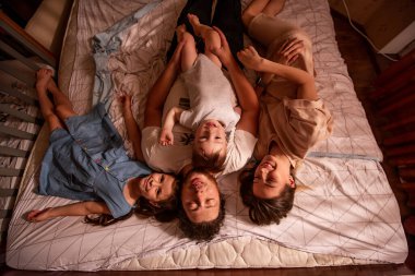 Sabahları yatakta uzanan neşeli bir ailenin en iyi görüntüsü. Tarz sahibi anne ve büyük kız babalarına her iki taraftan sarılırlar, bebek oğlan erkeğin karnında sürünür. Ev hayatı, yaşam tarzı.