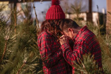 Kırmızı tişörtlü neşeli bir çift örgü örmüş şapkalar takıyor, yeşil Noel ağacı pazarında gülüyorlar. Genç adam gitmesine izin vermeden güzel bir kadının elini tutuyor. Tatil