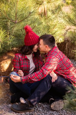 Kırmızı kareli gömlekli neşeli genç çift öpüşüyor, ormanda ellerinde neşeli maytaplar tutuyorlar. Erkek ve kadın Noel ağacı pazarında gülüyorlar. Mutlu aşıkların yakın plan portreleri. Yeni Yıl