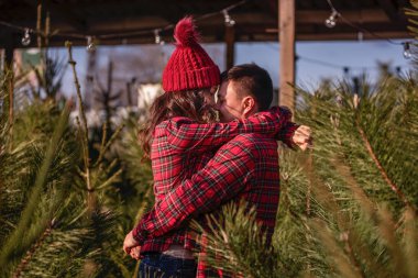 Kareli kırmızı gömlekli güzel bir çift, örgü şapkalı, yeşil Noel ağacı pazarında burun buruna sarılıyorlar. Genç adam gülüyor, muhteşem kadını öpüyor. Tatil atmosferi