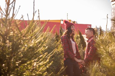 Kırmızı tişörtlü neşeli bir çift örgü örmüş şapkalar takıyor, yeşil Noel ağacı pazarında gülüyorlar. Genç adam gitmesine izin vermeden güzel bir kadının elini tutuyor. Tatil